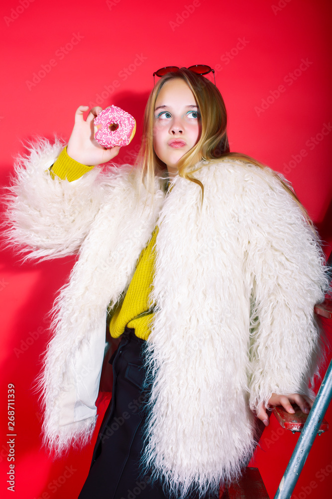 little cute blond teenage girl posing in fashion style with donut on red background, lifestyle people concept little cute blond teenage girl posing in fashion style with donut on red background, lifestyle people concept