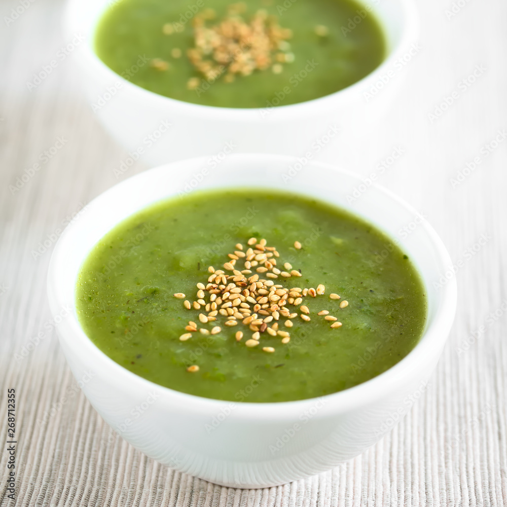 Fresh cream of zucchini soup with toasted sesame seeds on top served in bowls, photographed with natural light (Selective Focus, Focus in the middle of the first soup) Fresh cream of zucchini soup with toasted sesame seeds on top served in bowls, photographed with natural light (Selective Focus, Focus in the middle of the first soup)