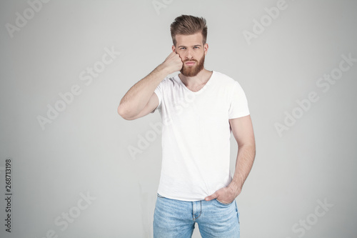 Portrait of beautiful sexy bearded man. He bends himself with his fist on the face. he stands in front of the white background