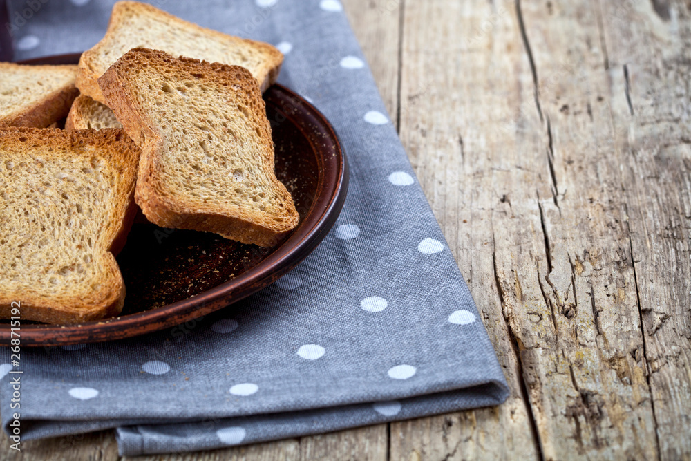 Toasted cereal bread slices on brown ceramic plate closeup on linen napkin on rustic wooden table background.