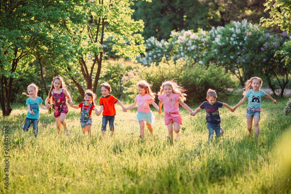 Obraz premium Large group of kids, friends boys and girls running in the park on sunny summer day in casual clothes .