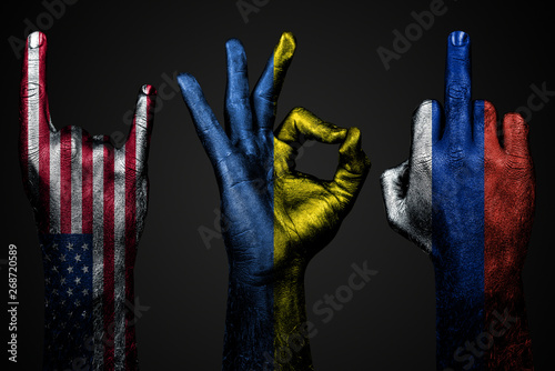 a set of three hands with a painted flag of Ukraine, Russia and USA show middle finger, goat and Okay, a sign of aggression, protest and approval on a dark background.