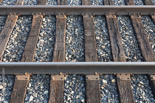 Steel railroad tracks cross wooden ties, and are set on top of a stone ballast surface, during a late afternoon day.