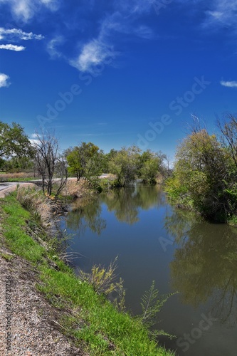 Jordan River Parkway Trail, Redwood Trailhead bordering the Legacy Parkway Trail, panorama views with surrounding trees and silt filled muddy water along the Rocky Mountains, Salt Lake City, Utah. 