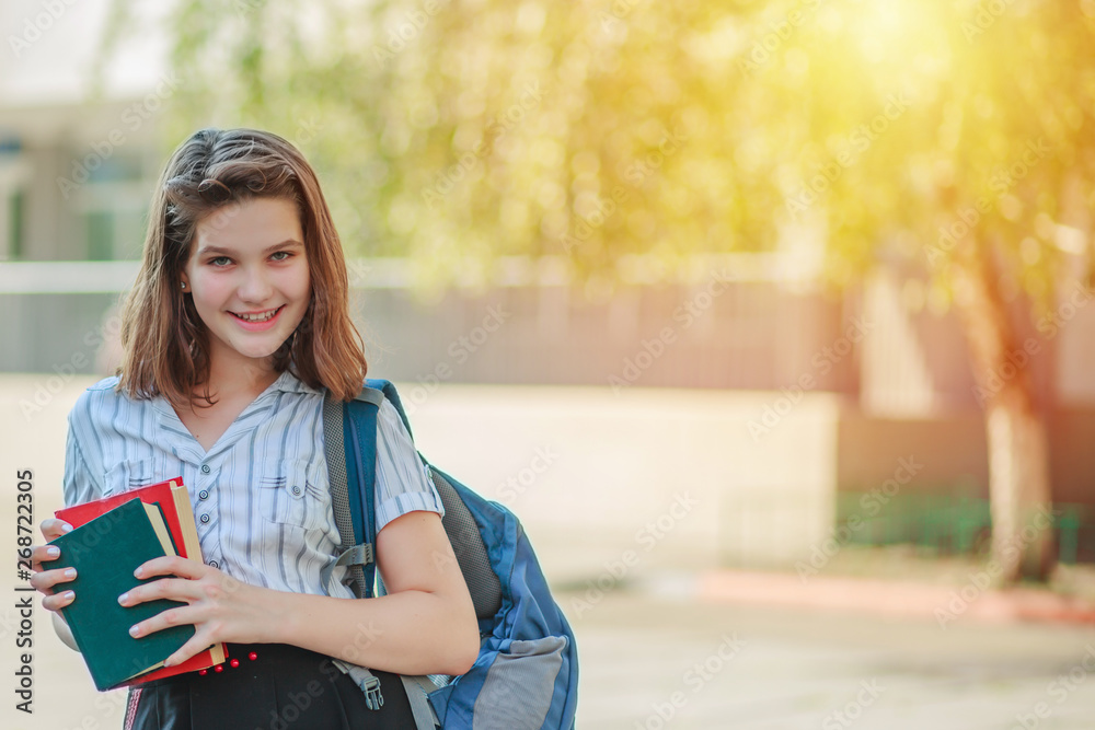 A girl holding two books red and green and smiling. Schoolgirl on the background of the school after the summer holidays. Ready to start the school year schoolgirl. A girl holding two books red and green and smiling. Schoolgirl on the background of the school after the summer holidays. Ready to start the school year schoolgirl.
