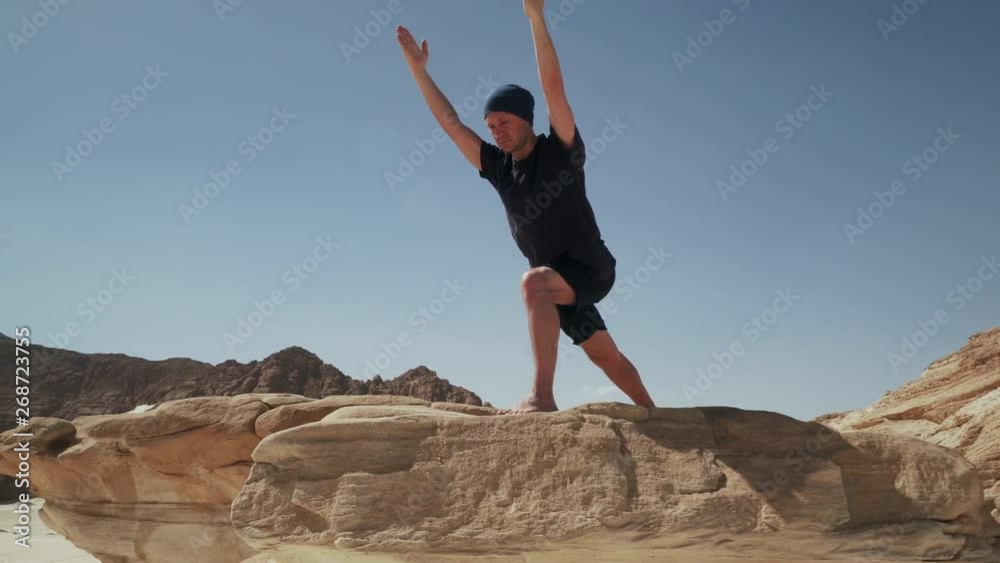 Handsome male doing yoga warrior pose on a rock in desert 4k Handsome male doing yoga warrior pose on a rock in desert 4k