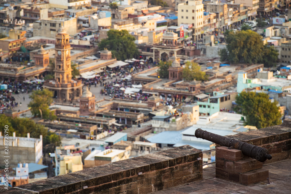 Stunning view of the Ghanta Ghar Clock Tower and the Sadar Market in the background and a cannon on the Mehrangarh fort in the foreground. Jodhpur, Rajasthan, India.