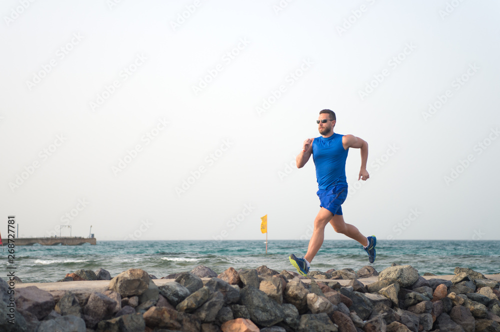 Pain is nothing compared to what it feels like to quit. Running man on beach. Runner training outdoors. Fit male sport fitness exercising in summer. Running sport and hobby. Man fitness coach