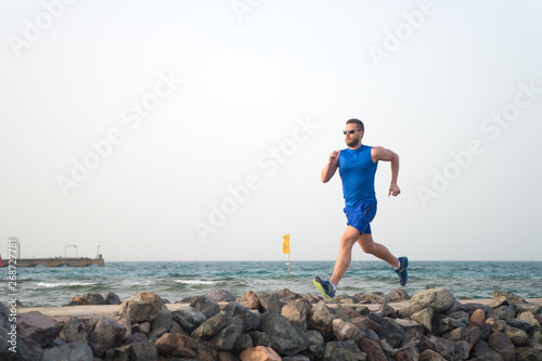 Pain is nothing compared to what it feels like to quit. Running man on beach. Runner training outdoors. Fit male sport fitness exercising in summer. Running sport and hobby. Man fitness coach © be free