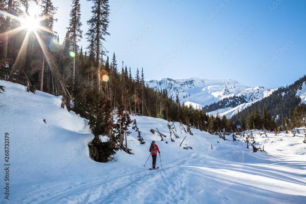 Skier hiking toward the Seven Steps of Paradise run down Young's Peak. The Asulkan Valley is lit by the morning sun around him.