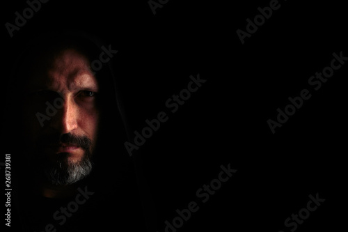 Brutal man with a gray beard in the hood with sharp shadows on a black background. Copy space.