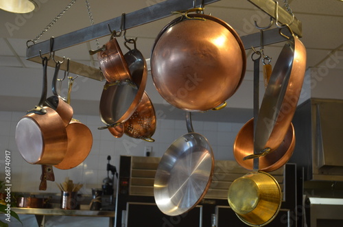 Copper kitchen cookware on an overhead rack.