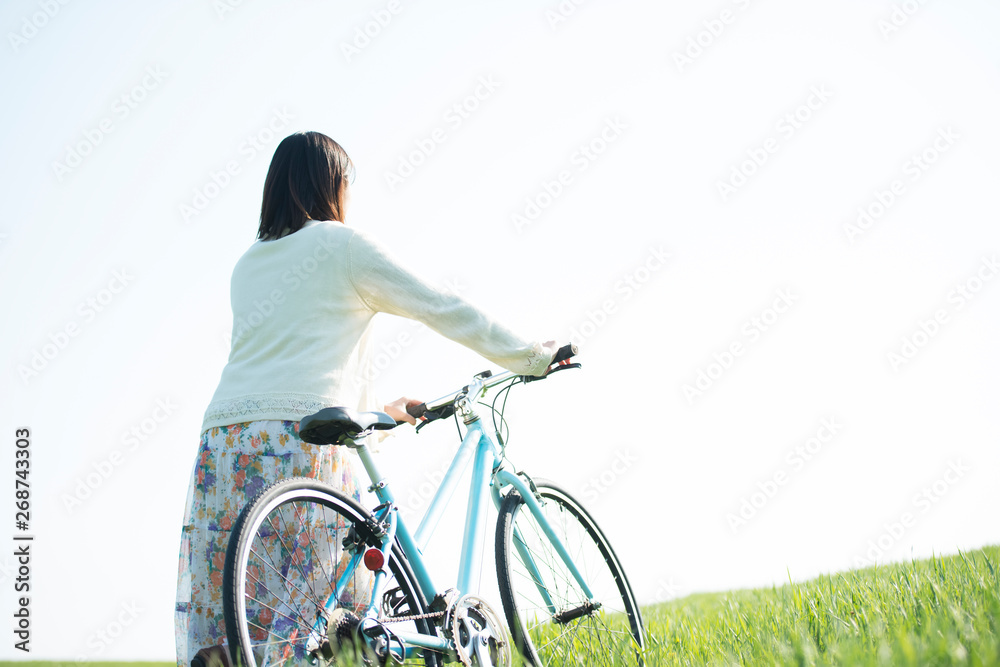 Obraz premium 草原で自転車を押す女性の後姿