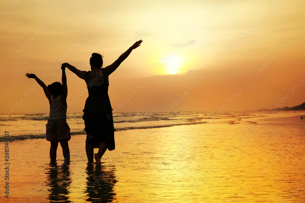 Mother and girl on the beach at sunset background
