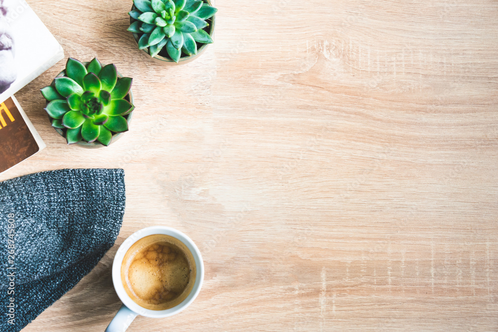 Top view of cosy home scene. Books, woolen blanket, cup of coffee and succulent plants over wooden background. Copy space.