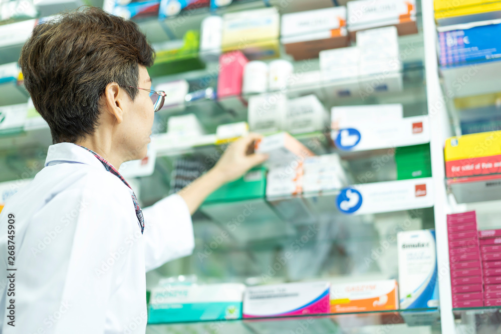 senior Asian pharmacist hand holding medicine box for client or patient in pharmacy drugstore. concept of service, pharmacy drugstore, healthcare,life and people senior Asian pharmacist hand holding medicine box for client or patient in pharmacy drugstore. concept of service, pharmacy drugstore, healthcare,life and people