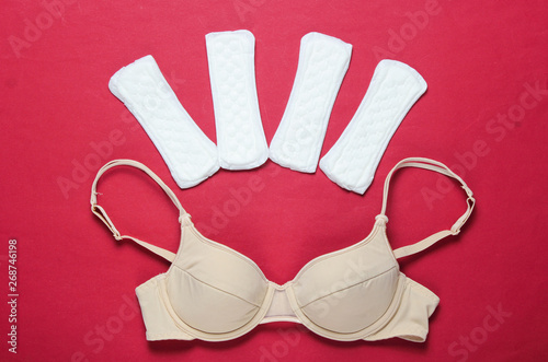 Women's critical days, menstruation. Minimalistic feminine hygiene concept. Beautiful sexy bra, panty liners on red background. Top view