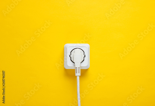 White cable plugged into power outlet on yellow wall background