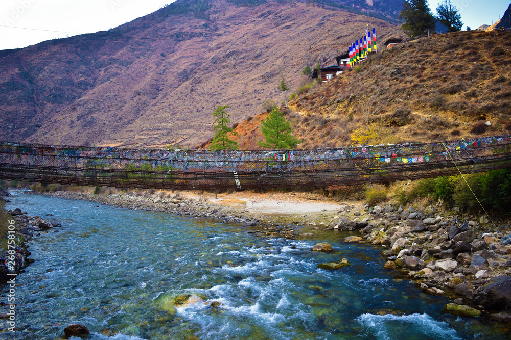 side view of walking suspension bridge with a lot of colorful prayer flags in Bhutan.
