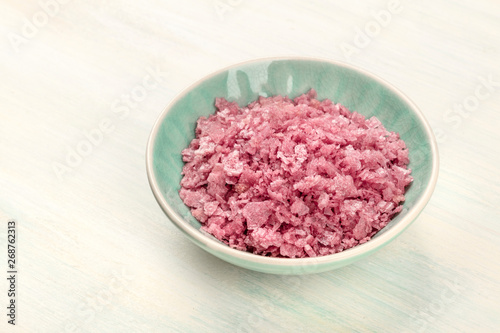 A bowl of pink Himalayan sea salt on a white wooden background with a place for text