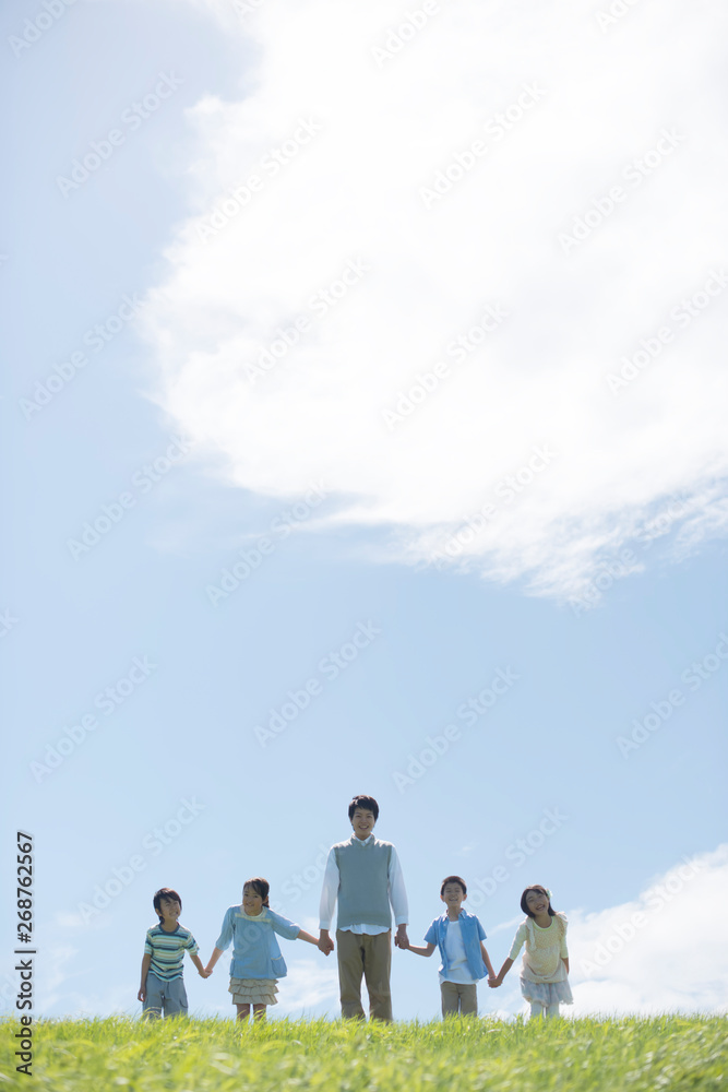 Fototapeta premium 草原で手をつなぐ小学生と先生