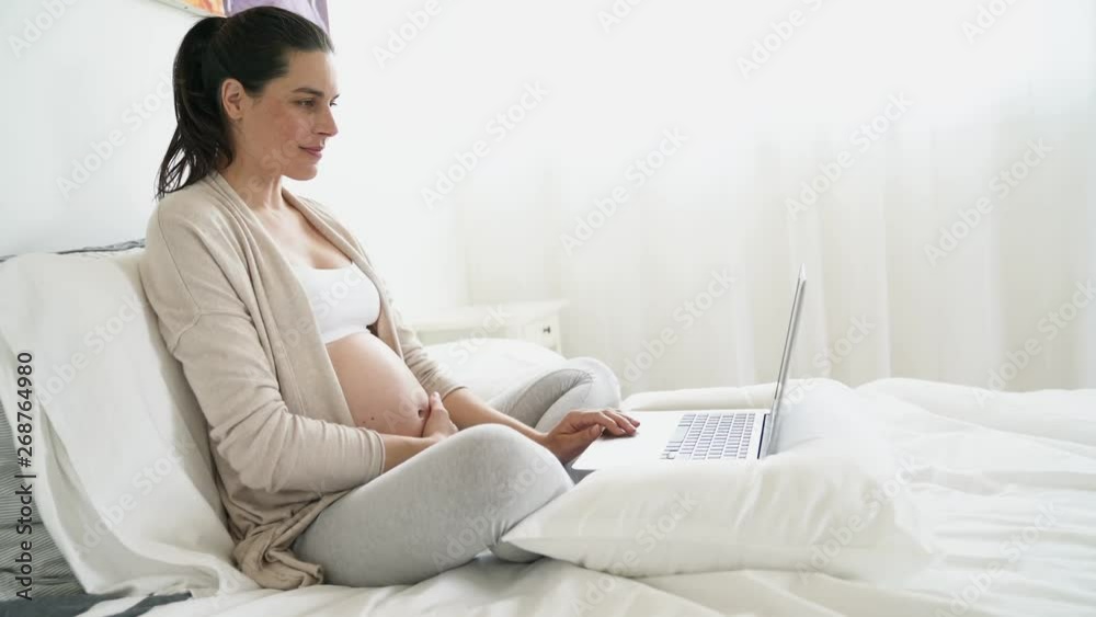 Pregnant woman relaxing on bed, using laptop