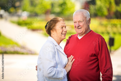 Cheerful senior couple having good time in city park, walking, laughing and enjoying sunny day