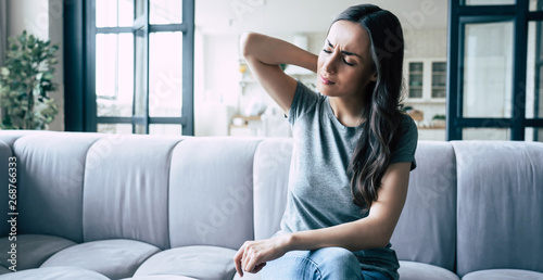 Severe woman pain in head and neck while sitting on the couch at home photo