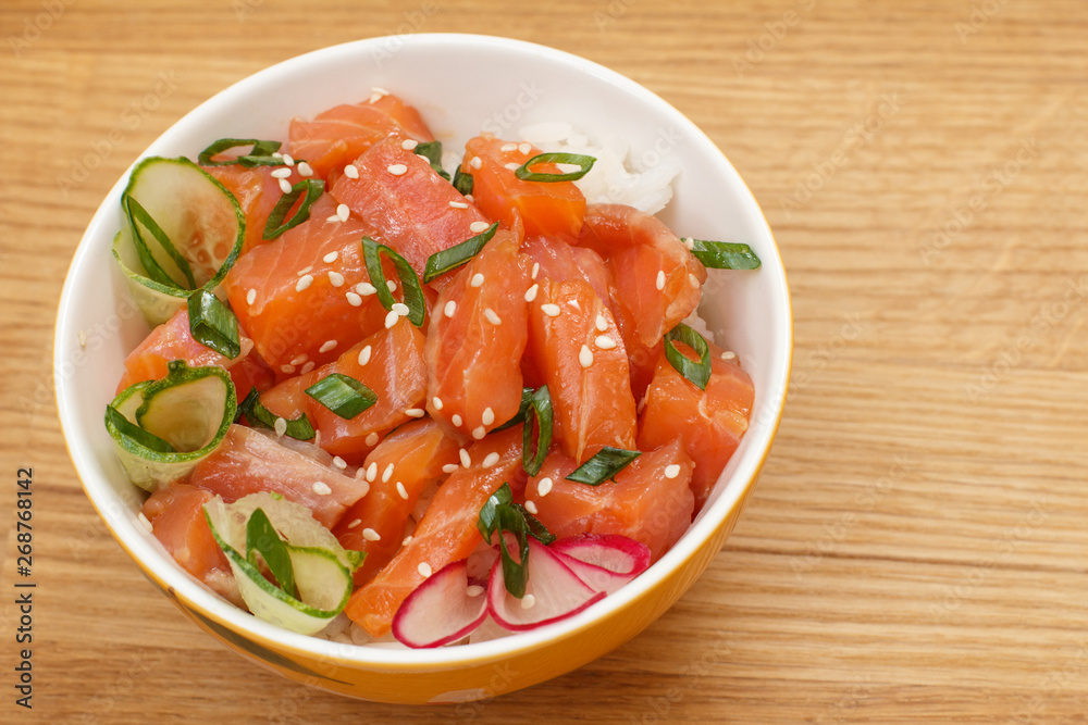 Hawaiian poke with salmon and sesame seeds, boiled rice, fresh cucumber, radish and green onions in glass bowl. Hawaiian poke with salmon and sesame seeds, boiled rice, fresh cucumber, radish and green onions in glass bowl.