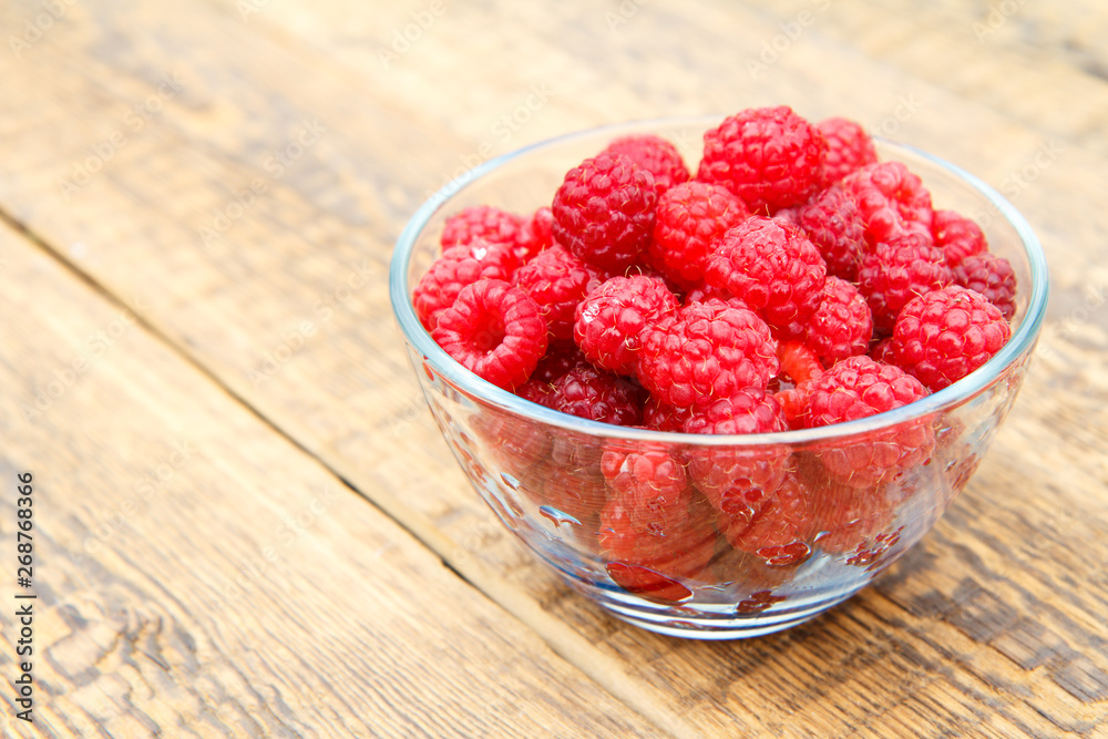 Ripe raspberries in the glass bowl on wooden boards. Ripe raspberries in the glass bowl on wooden boards.