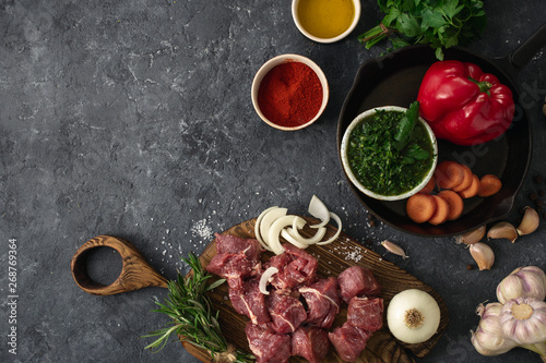 Ingredients for cooking meat with vegetables on a dark background top view. Preparation beef meat