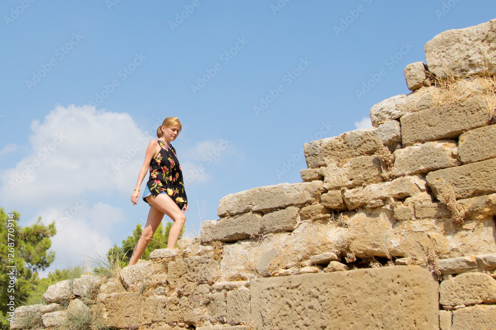 The concept of a summer holiday, active and historical. Tanned blond girl rises and the top of the ancient ruins in Turkey. Bright midday sun.