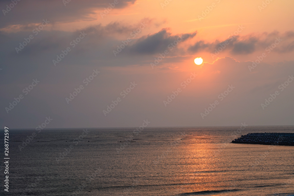 Fototapeta premium Seascape at Yellow glowing sun setting in the horizon with breakwater.