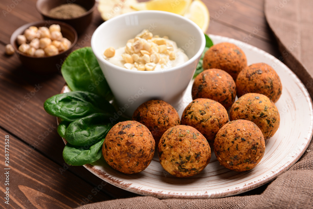 Plate with tasty falafel balls and sauce on wooden table