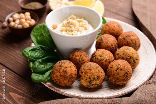 Plate with tasty falafel balls and sauce on wooden table