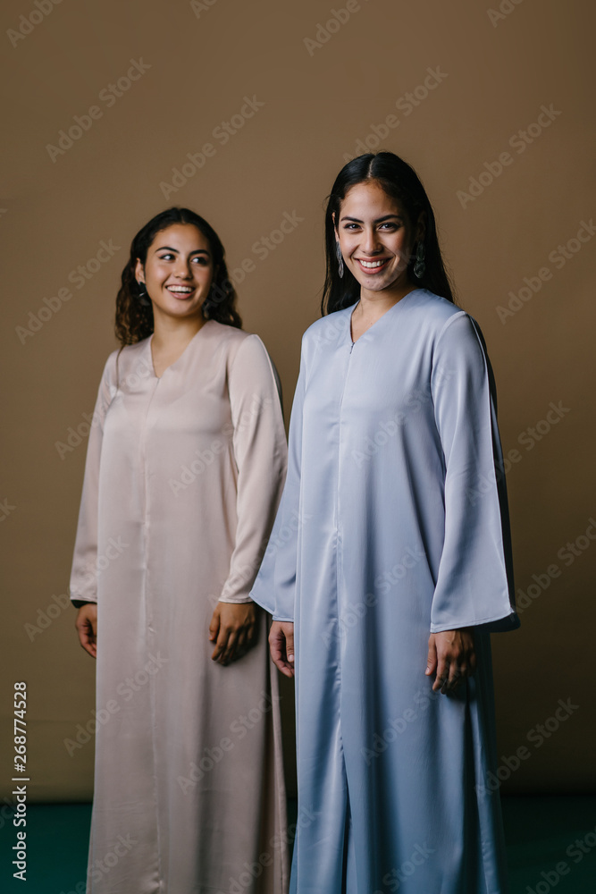 Portrait of two young Middle Eastern Muslim women smiling as they pose for their photo. They are wearing traditional pastel coloured Baju Kurung dresses to visit during Raya. 
