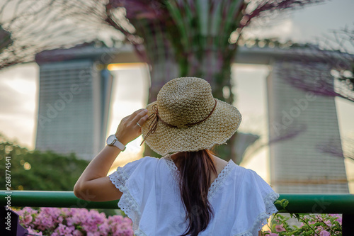 Young Woman traveling with white dress and hat, Asian traveler looking to supertree at gardens by the bay in Singapore. landmark and popular for tourist attractions. Southeast Asia Travel concept