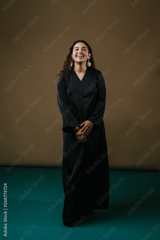 Studio portrait of a beautiful and attractive Malay Asian woman in a traditional black baju kurung dress against a brown background. She is dancing and smiling as she poses for her photo. Studio portrait of a beautiful and attractive Malay Asian woman in a traditional black baju kurung dress against a brown background. She is dancing and smiling as she poses for her photo.