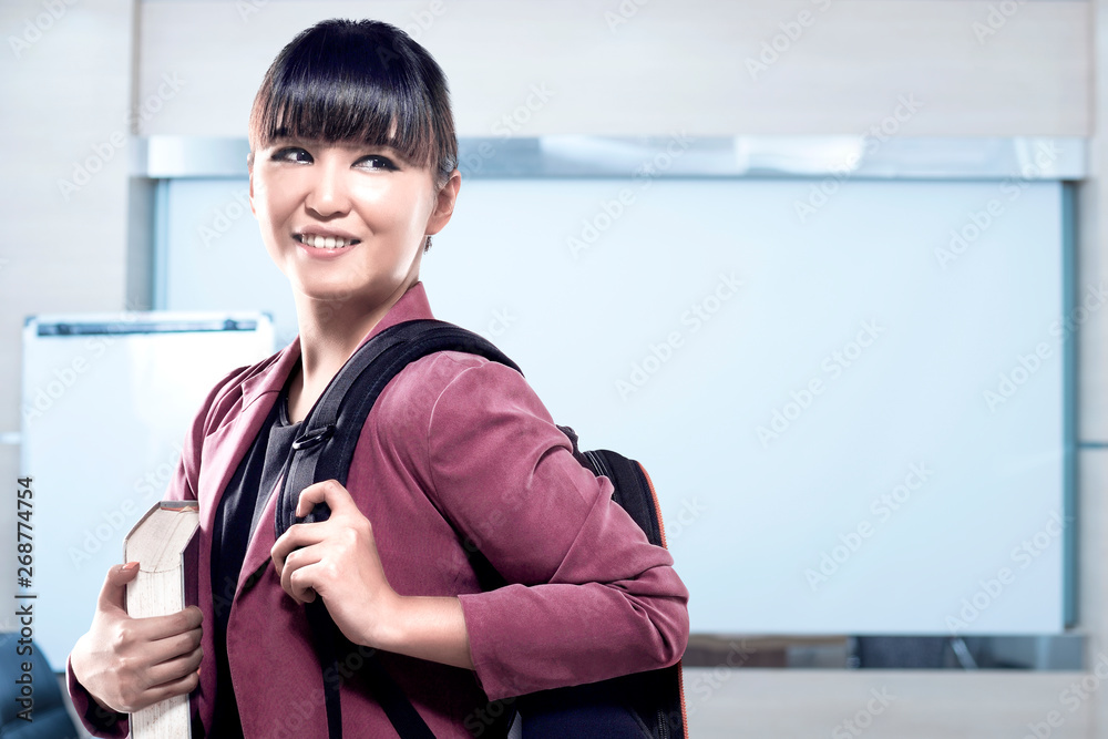 Asian student woman with backpack carrying book standing and look back in the classroom with whiteboard