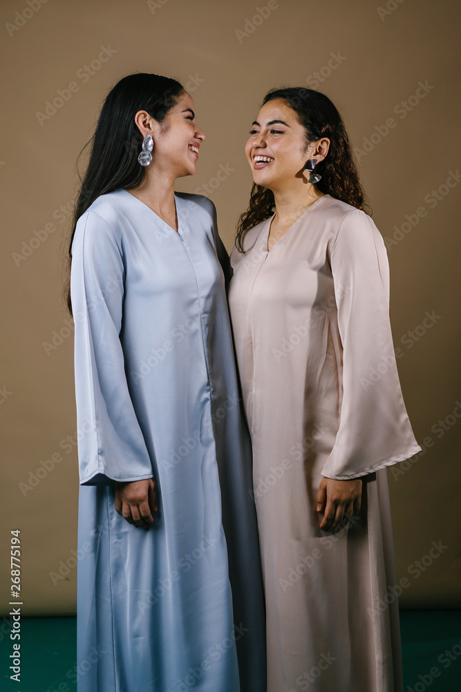 Portrait of two young Middle Eastern Muslim women smiling as they pose for their photo. They are wearing traditional pastel coloured Baju Kurung dresses to visit during Raya. Portrait of two young Middle Eastern Muslim women smiling as they pose for their photo. They are wearing traditional pastel coloured Baju Kurung dresses to visit during Raya.