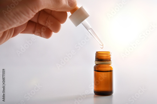 Hand with pipette and brown glass container with medication