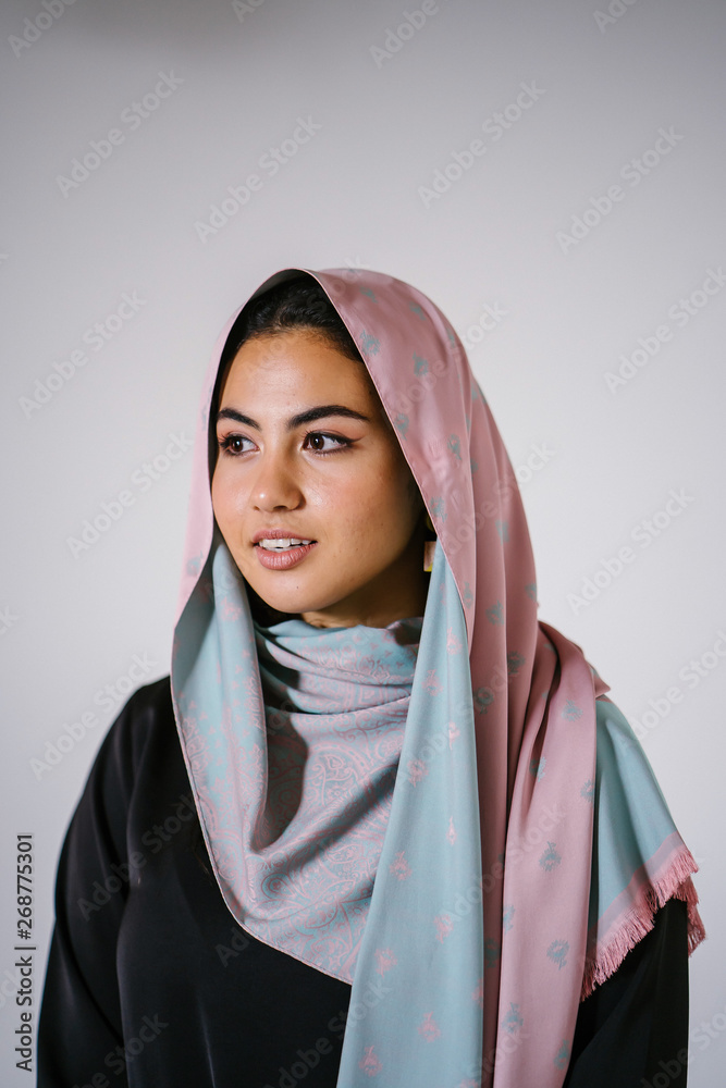 Studio portrait of a beautiful, young and attractive Middle Eastern woman  in a traditional black dress and colorful head scarf shawl for Raya (Eid)  against a white background. Stock Photo | Adobe