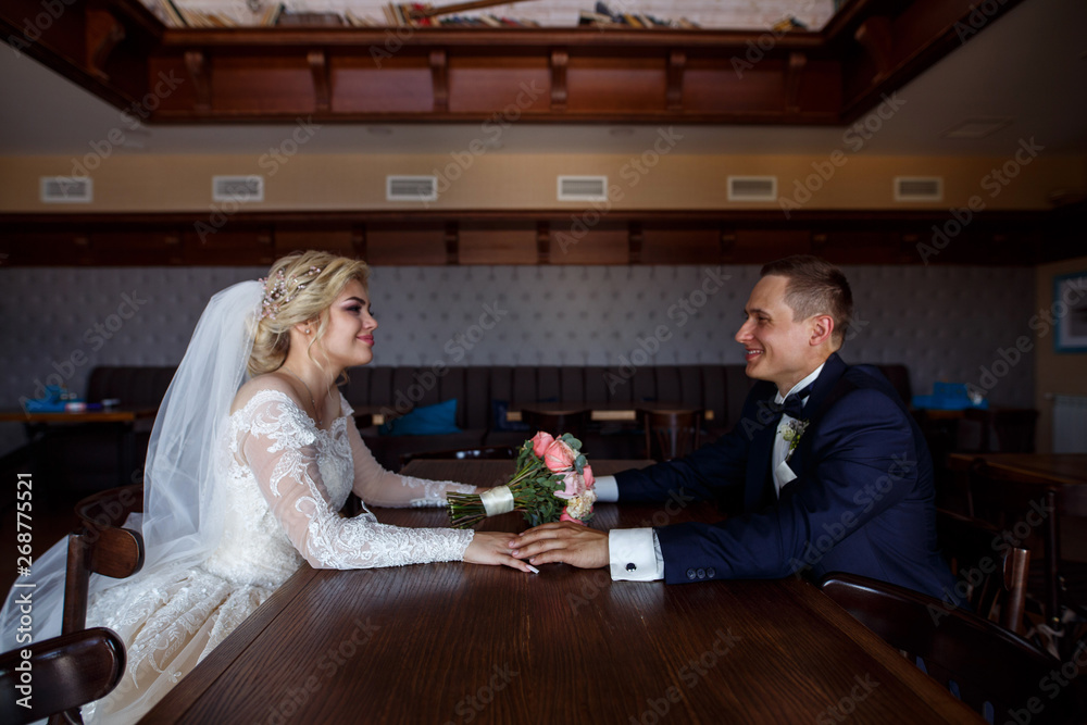 bride and the groom hold hands. portrait of a loving newlyweds in a beautiful interior.the brides gently look at each other indoor. wedding day. wedding concept. bride and the groom hold hands. portrait of a loving newlyweds in a beautiful interior.the brides gently look at each other indoor. wedding day. wedding concept.
