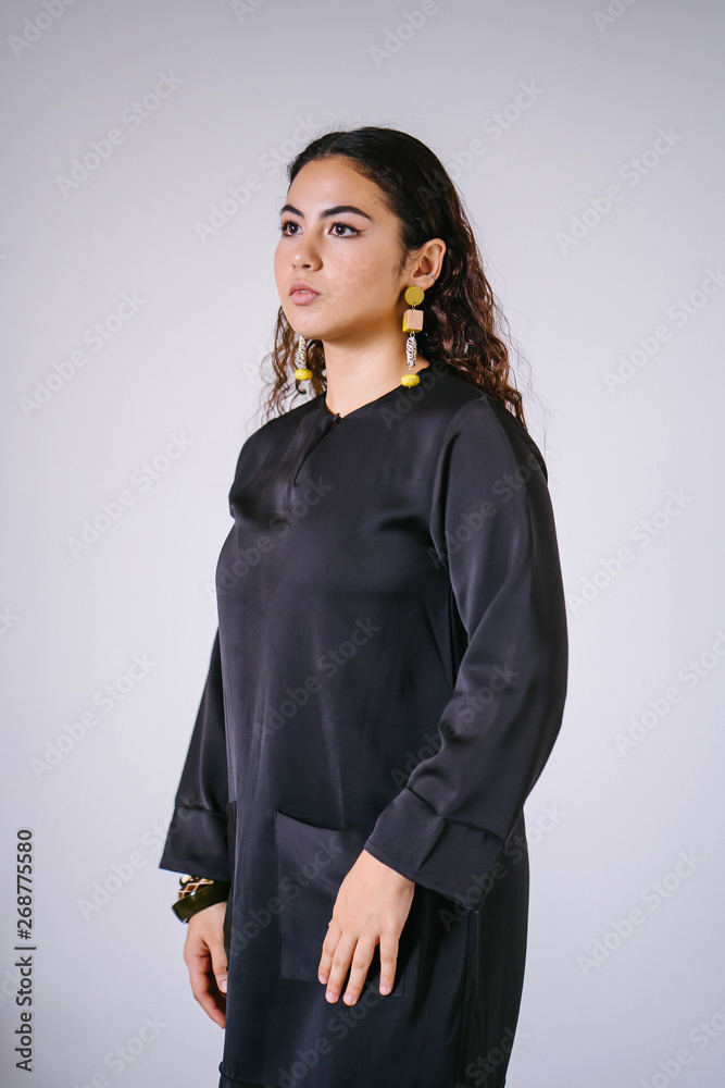 Studio portrait of a beautiful, young and attractive Malay Asian woman in a traditional black dress (Baju Kurung) for Raya (Eid) against a white background. She is youthful and radiant. Studio portrait of a beautiful, young and attractive Malay Asian woman in a traditional black dress (Baju Kurung) for Raya (Eid) against a white background. She is youthful and radiant.