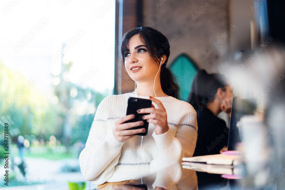 Young woman sitting cafe at table, thoughtfully looking out window, holding smartphone.Portrait girl with cell phone in her hands. Young woman sitting cafe at table, thoughtfully looking out window, holding smartphone.Portrait girl with cell phone in her hands.