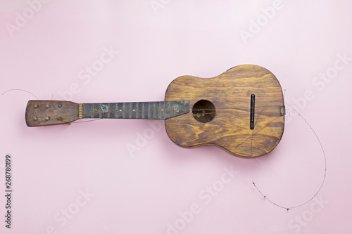 Old wooden guitar with torn strings. Soft pink background