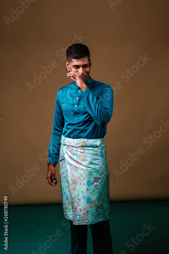 Studio portrait of a young, handsome and athletic Malaysian Indian Muslim Asian man in a blue traditional baju melayu tunic. He is smiling and looks happy and relaxed as he poses for his head shot.  photo