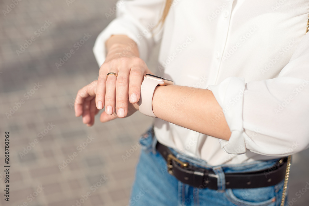Woman wearing white shirt wearing blue jeans and a gentle nude manicure looks at the watch close-up