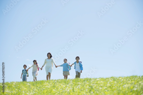 草原で手をつなぐ小学生と先生 © ohayou!