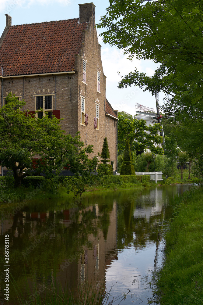 Old traditional Dutch house and mill along a river with reflection in the Netherlands